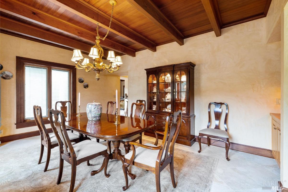 Elegant dining room with a polished wooden table, matching chairs, a chandelier, and a glass display cabinet.