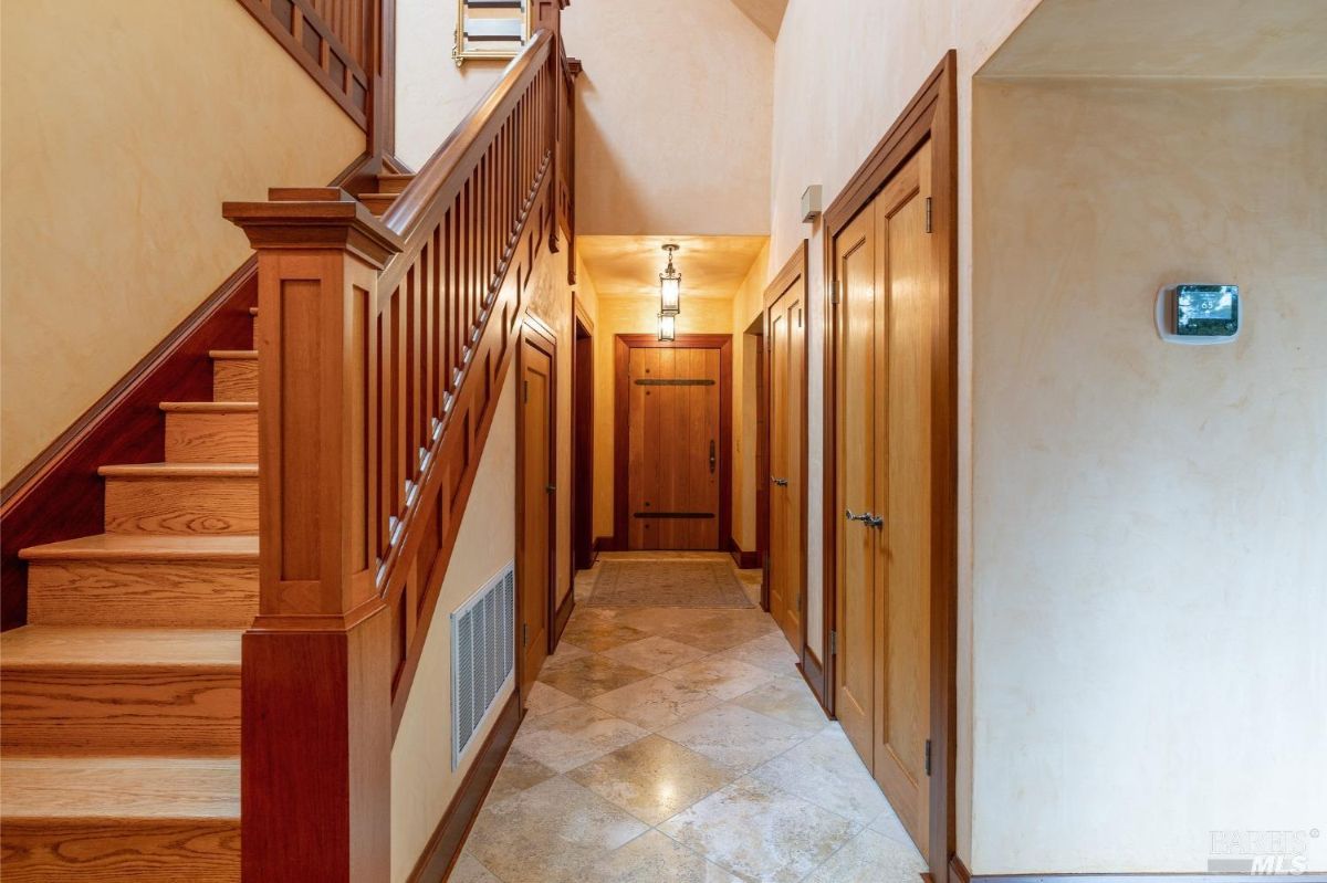 Bright hallway showcasing a wooden staircase, tiled flooring, and doors leading to various rooms.