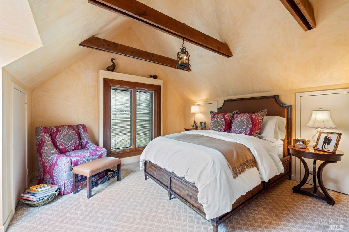 Warm and inviting attic bedroom with vaulted ceilings, exposed beams, and vibrant upholstery accents.