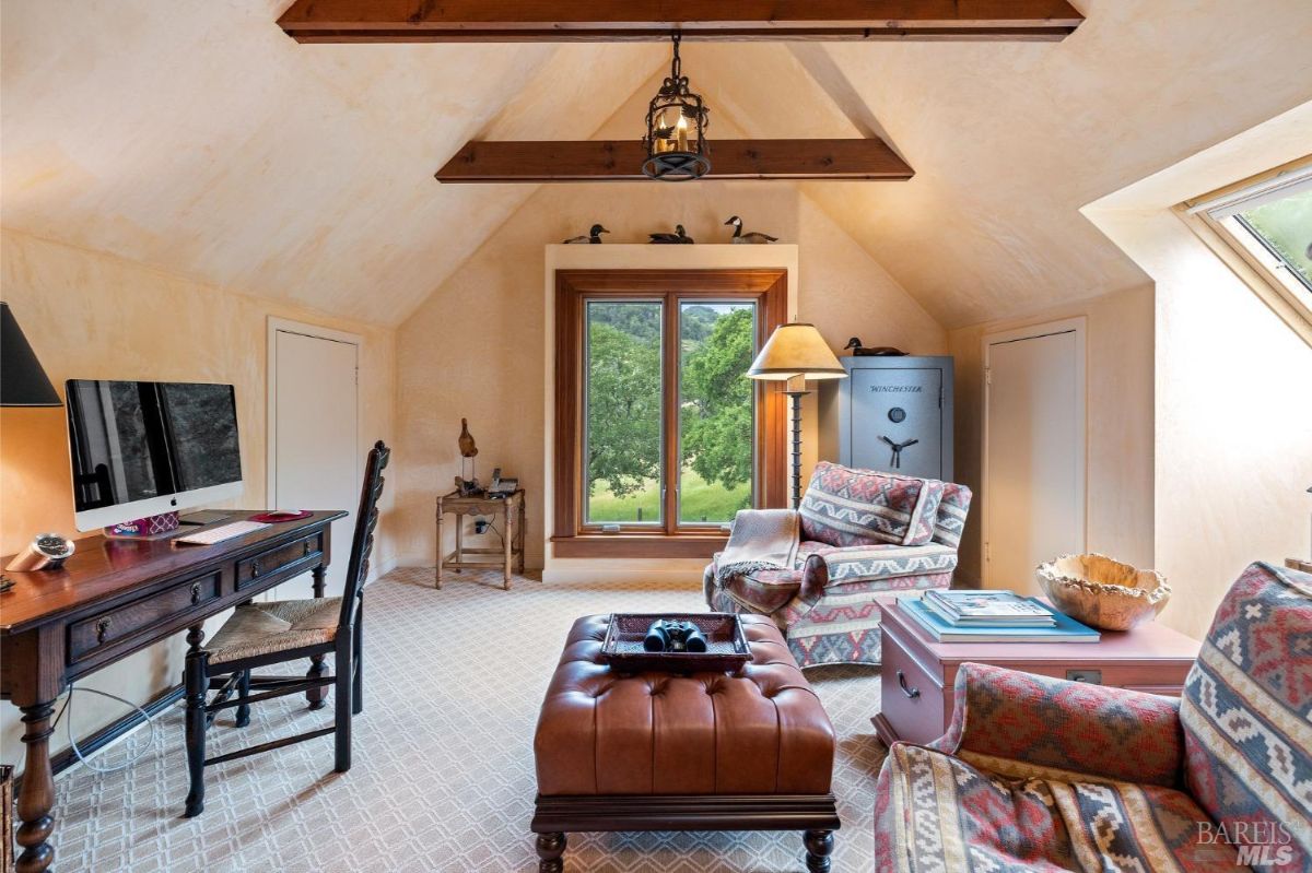 A bright workspace with a pitched ceiling, rustic beams, a scenic window view, and comfortable seating.