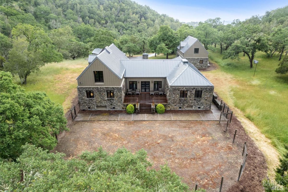 Home exterior highlights a modern farmhouse design with stone walls and metal roofing surrounded by greenery.