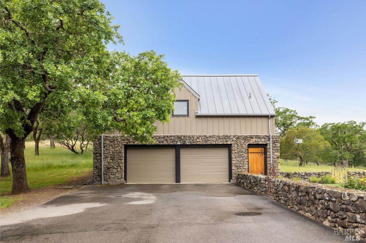 Detached garage with a stone facade and metal roof sits adjacent to a spacious driveway.