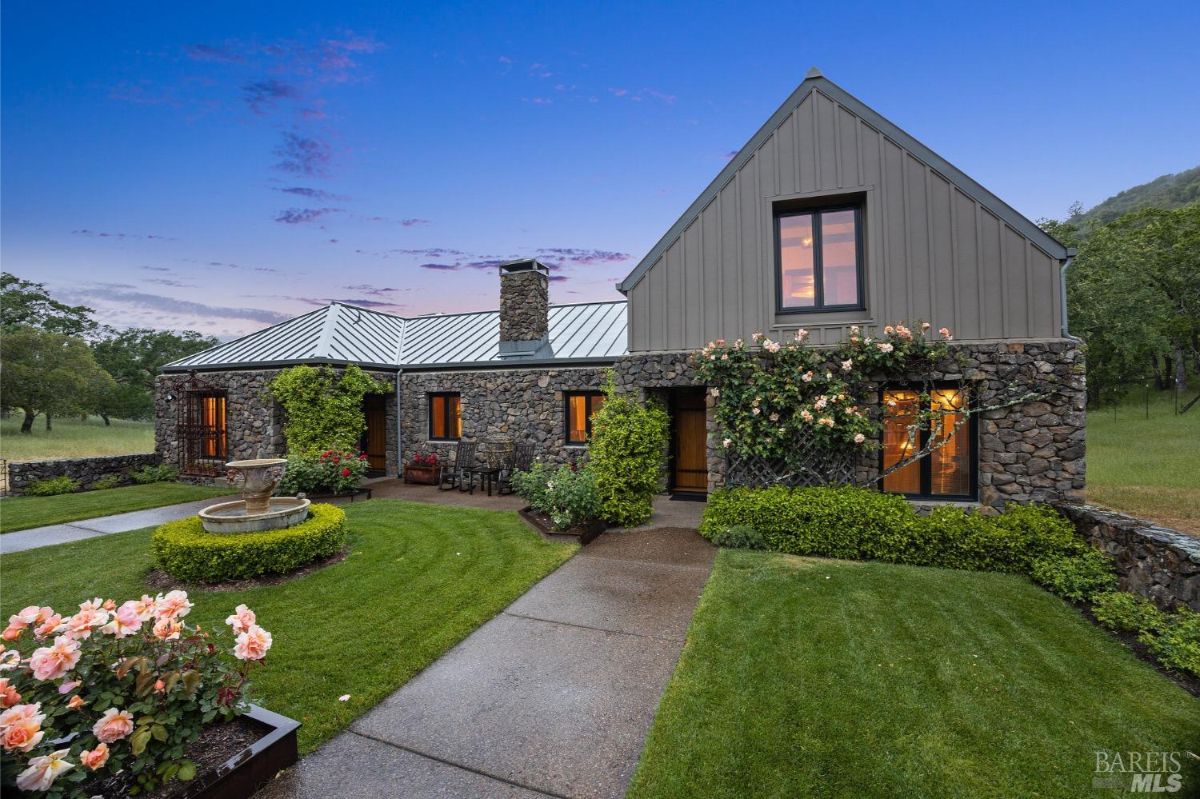 The stone home captured at twilight, highlighting its charming design, well-maintained garden, and ambient lighting.