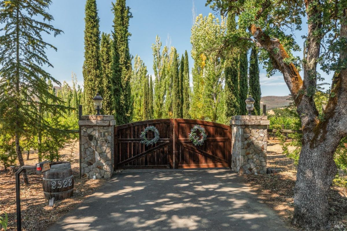 Stone and wood gated entry surrounded by tall cypress trees and rustic decorations.