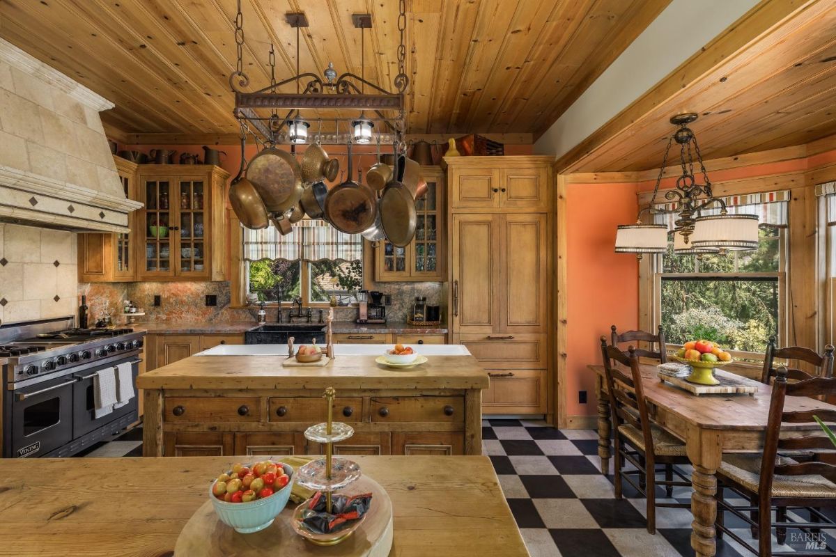 Country-style kitchen with a central island, hanging pots, and large wooden cabinetry.