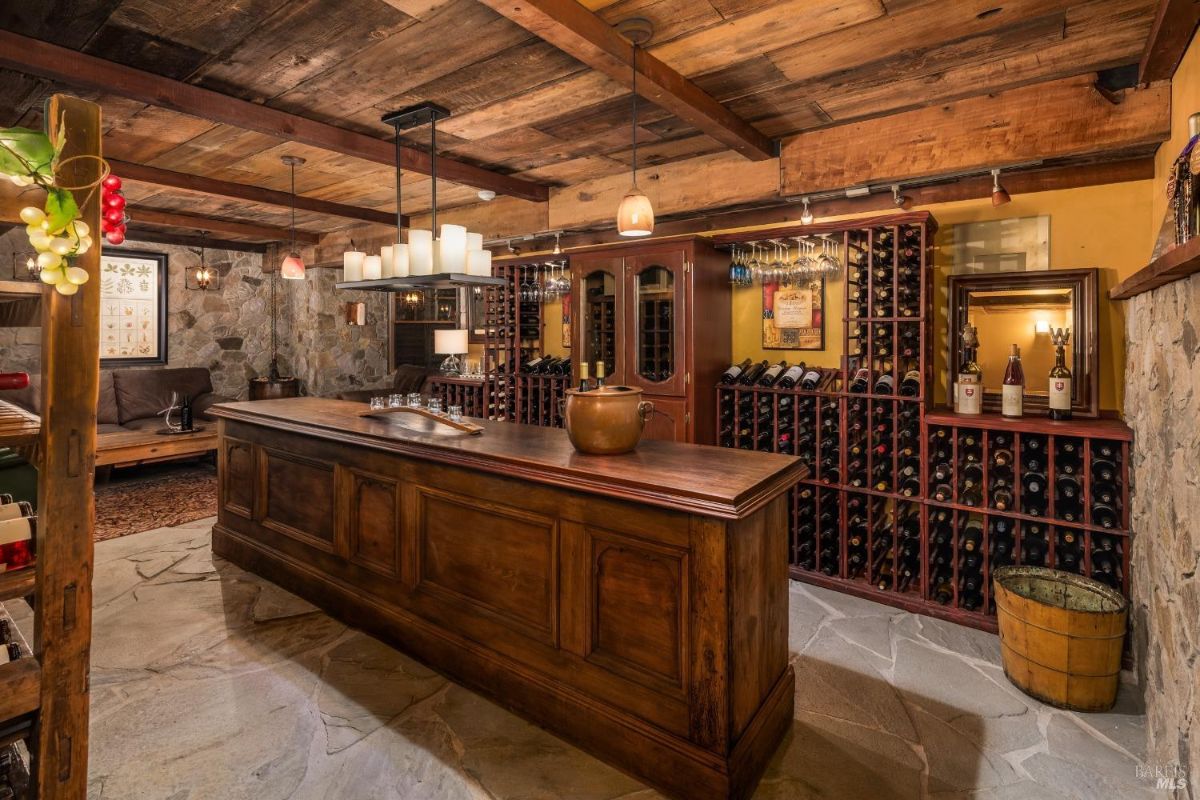 Wine cellar has a stone wall, wood ceiling, bar, wine racks, and a chandelier.