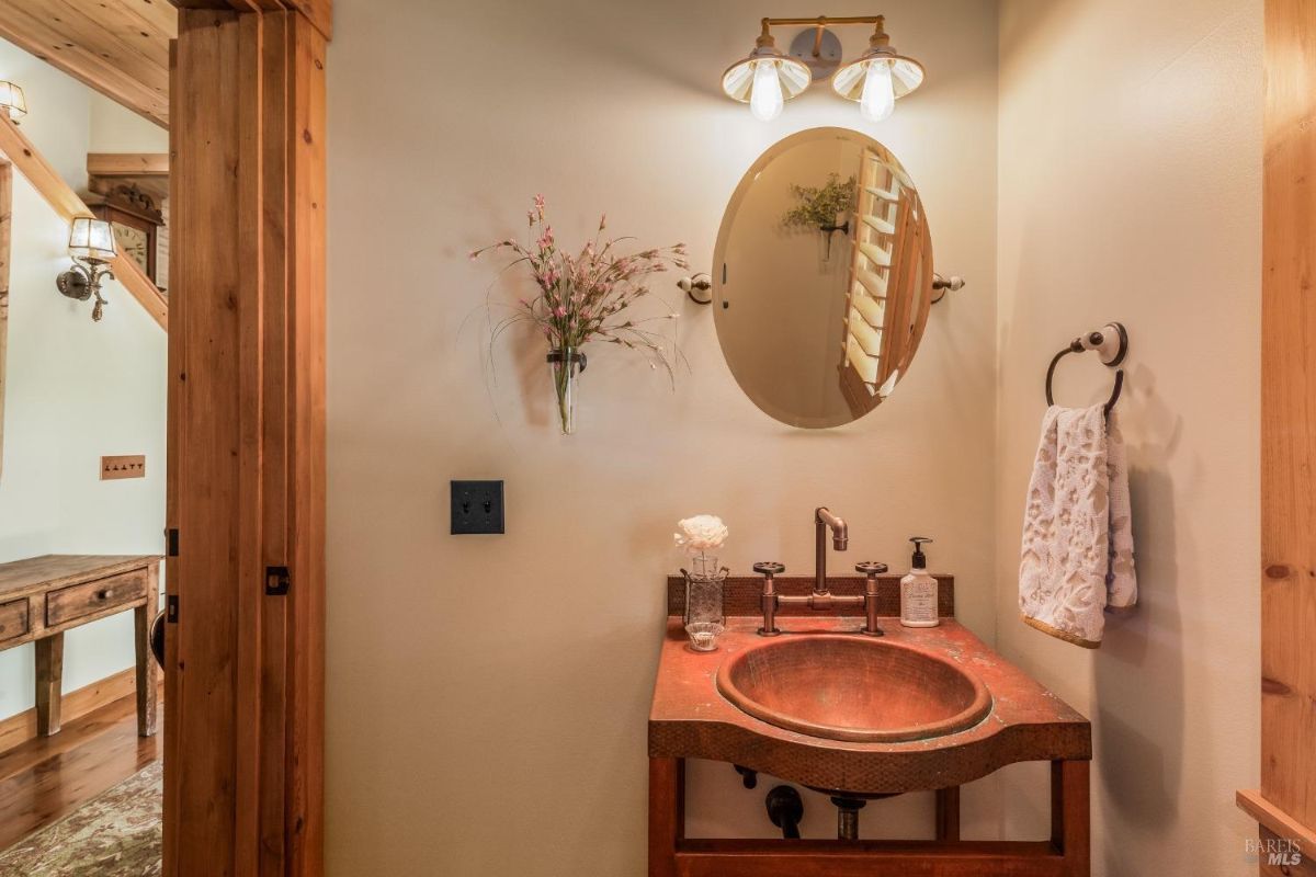 Small bathroom or powder room has a copper sink, oval mirror, and single light fixture.