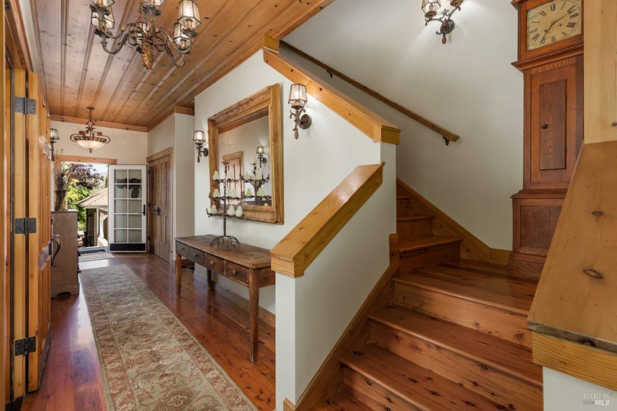 Hallway featuring a wooden staircase, antique furnishings, and decorative chandeliers.