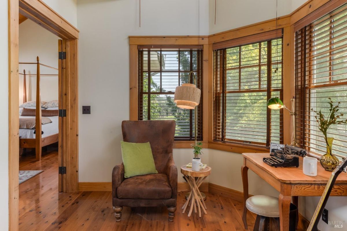 Cozy reading nook with a leather armchair, wooden desk, and large windows.