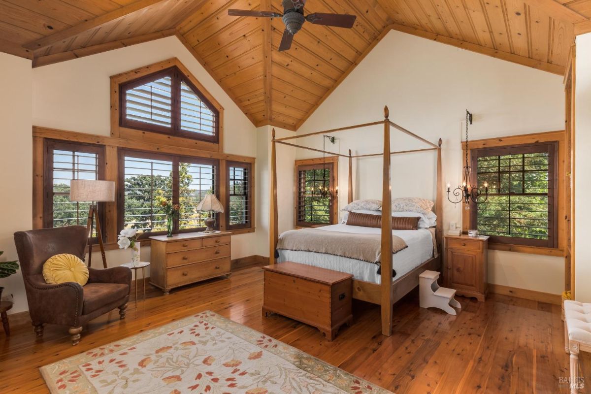 Bedroom features a vaulted wood-paneled ceiling, a four-poster bed, wooden furniture, and multiple windows.