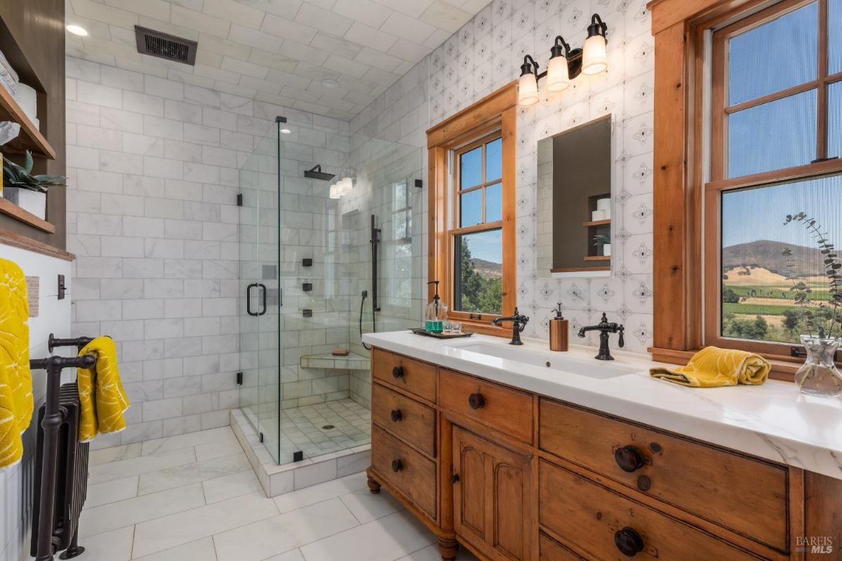 Bathroom has a walk-in shower, double vanity with wooden cabinets, and two windows with views.