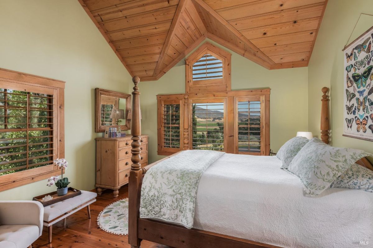 Bedroom has wood-paneled vaulted ceilings, a four poster bed, wood furniture, and a framed butterfly collection.