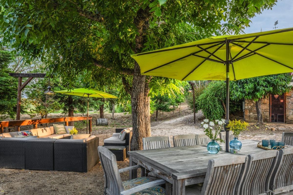 Outdoor space has a dining table, chairs, patio furniture, umbrellas for shade, and a gravel ground covering.