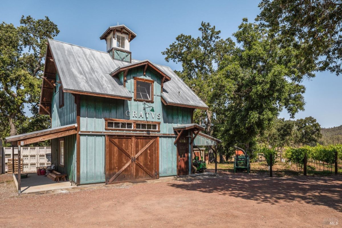 Large barn with a cupola stands next to a vineyard.