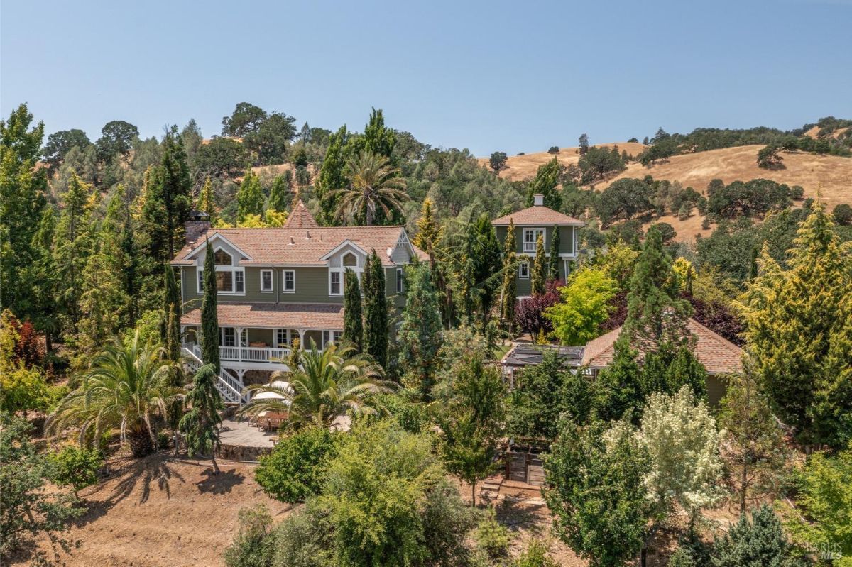 Large house with multiple stories and a turret is surrounded by trees.