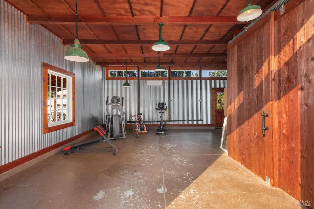 Home gym has wood ceiling, corrugated metal walls, exercise equipment, and sliding barn doors.