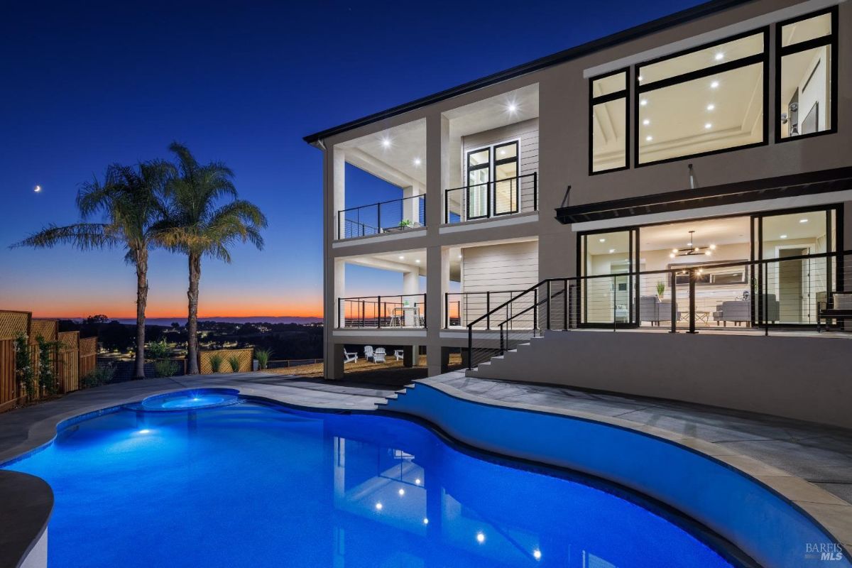 Illuminated modern home exterior with a vibrant pool under the night sky.