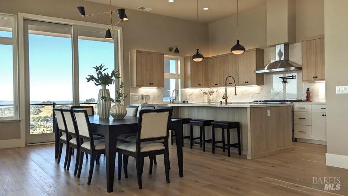 Dining area connected to a modern kitchen with panoramic windows and elegant lighting.