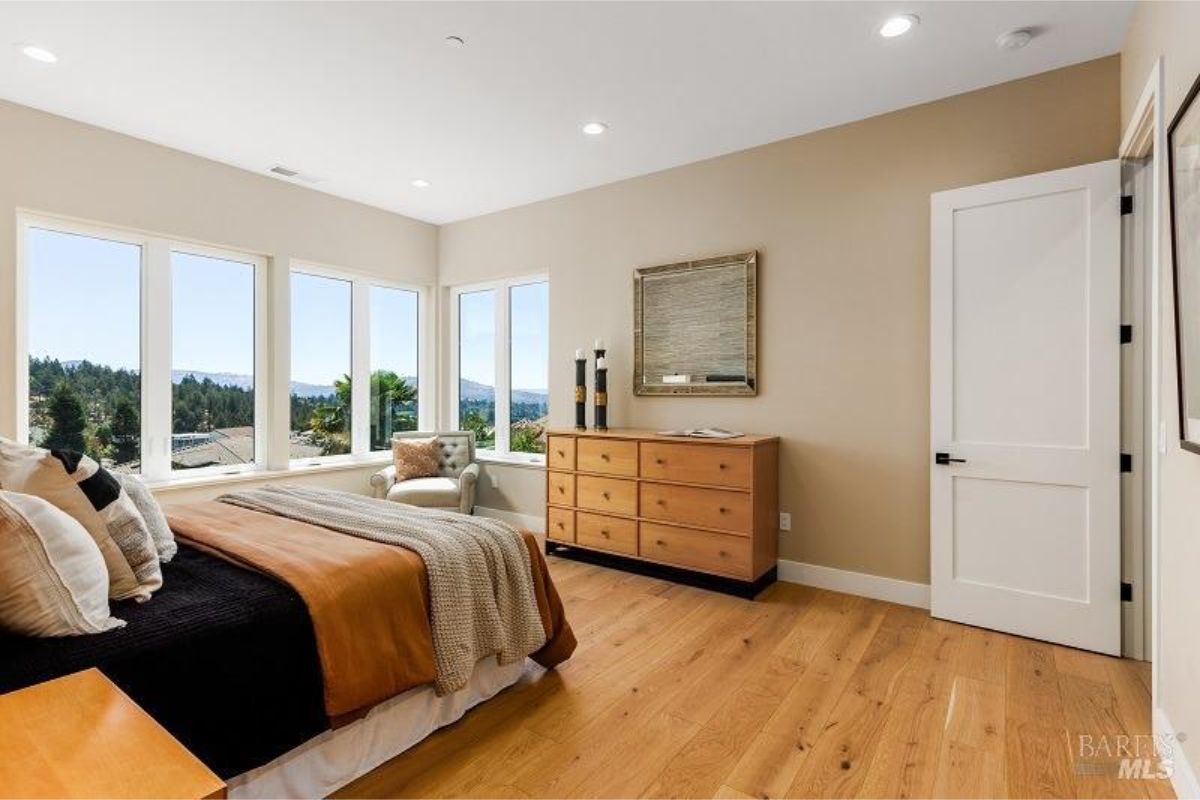 Spacious bedroom with large windows offering scenic views and warm wood flooring.