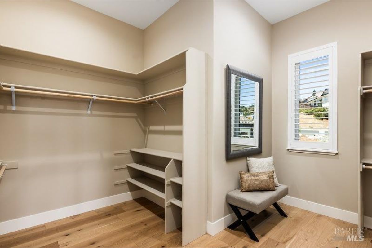 Organized walk-in closet with open shelving, racks, and a small seating area.