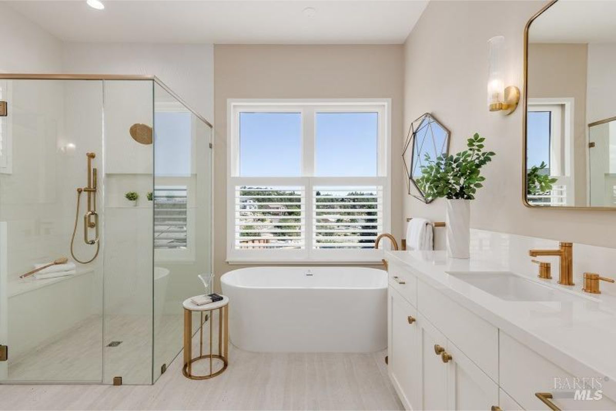 Luxurious bathroom featuring a free-standing bathtub, glass shower, and gold accents.