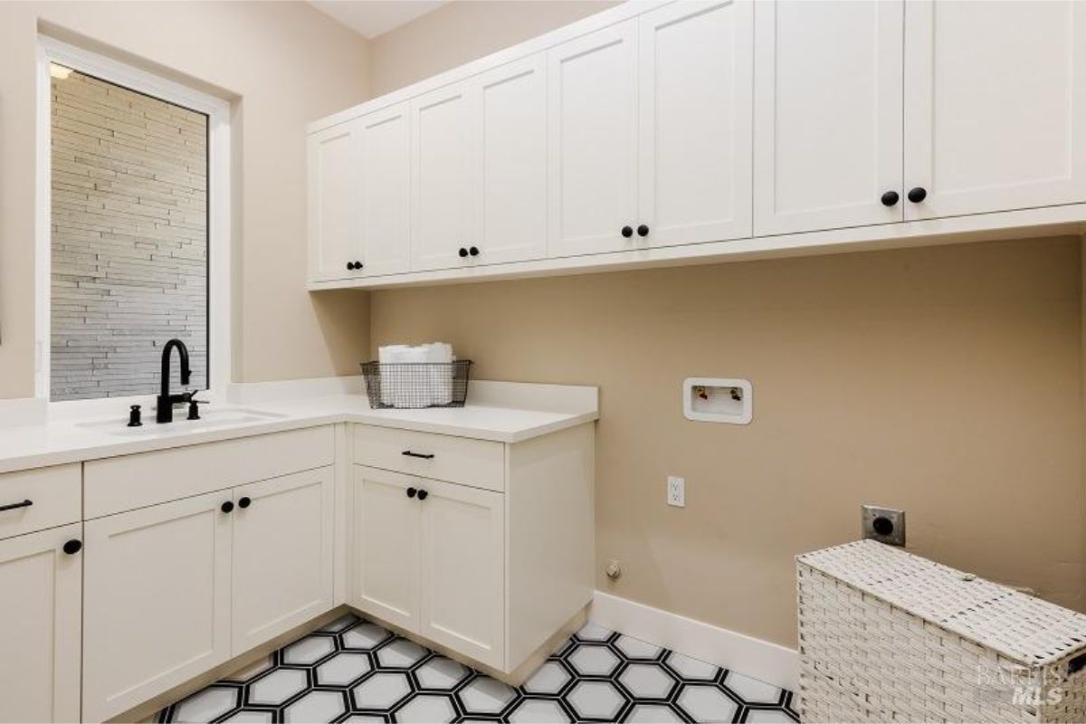 Laundry room has white cabinets, black hardware, and a patterned tile floor.