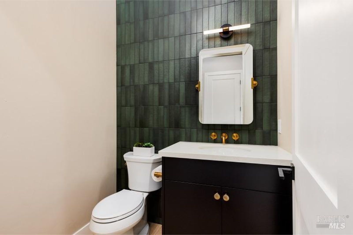 Bathroom has green tile, black vanity, gold fixtures, and a mirror.