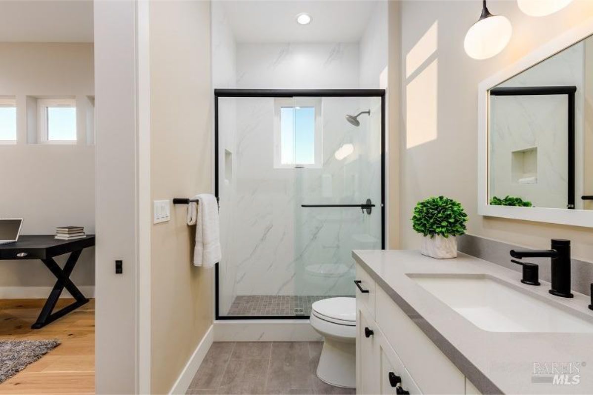 Bathroom has a walk-in shower with marble tile, a single vanity, and black fixtures.