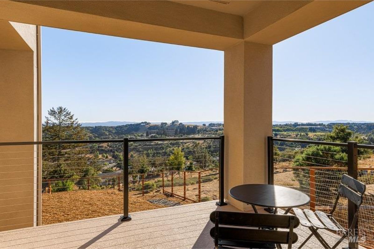 Balcony has a table, two chairs, and a view of hills and trees.