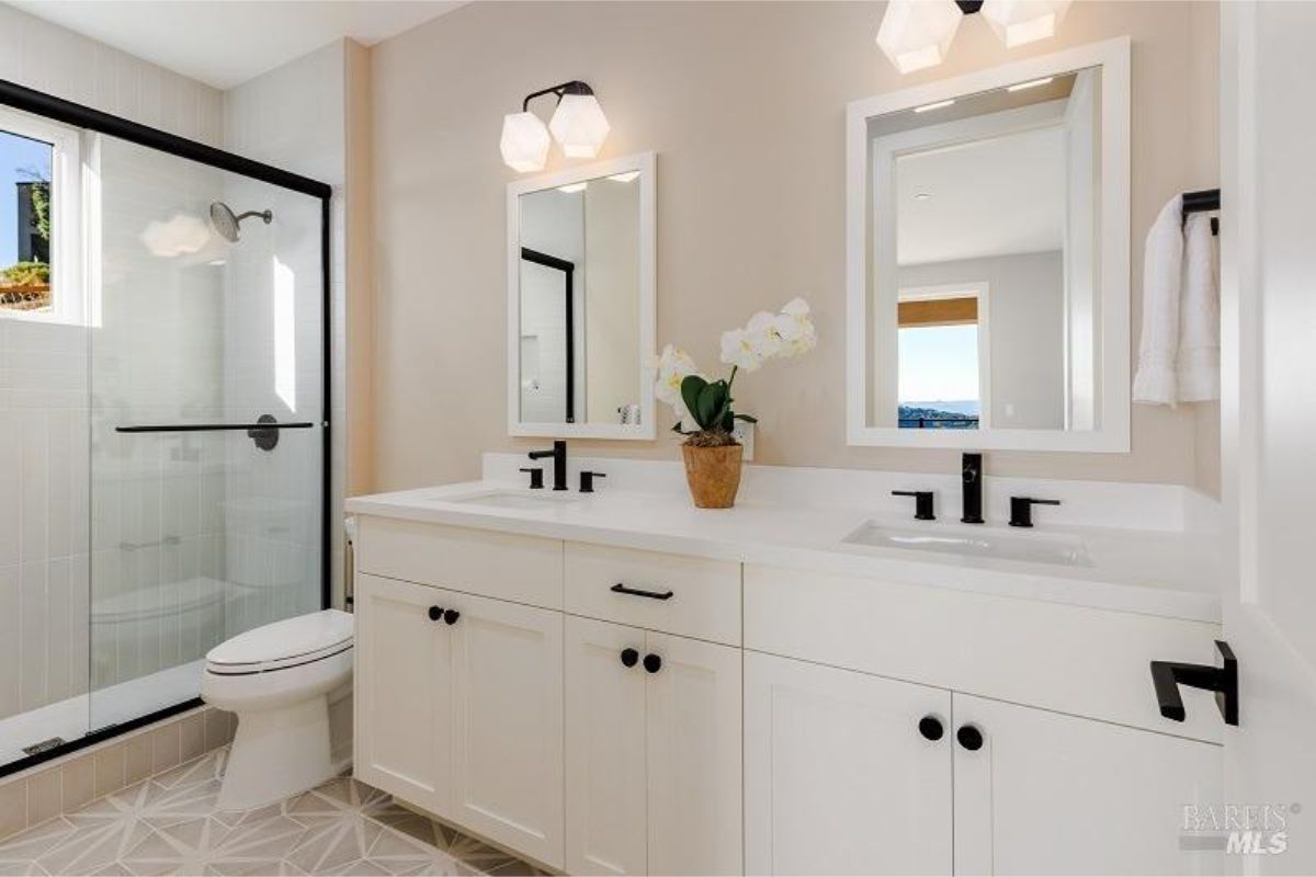 Bathroom has a walk-in shower, double vanity with white cabinets, and black fixtures.