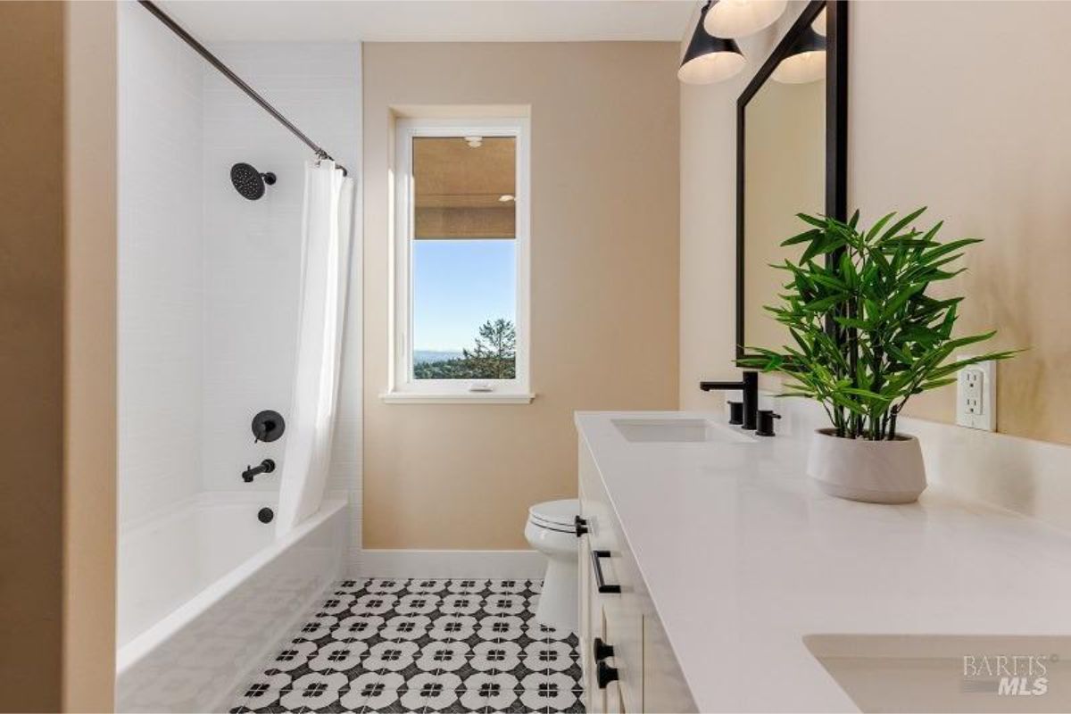 Bathroom has a bathtub/shower combination, double vanity with white countertop, black fixtures, and a patterned tile floor.