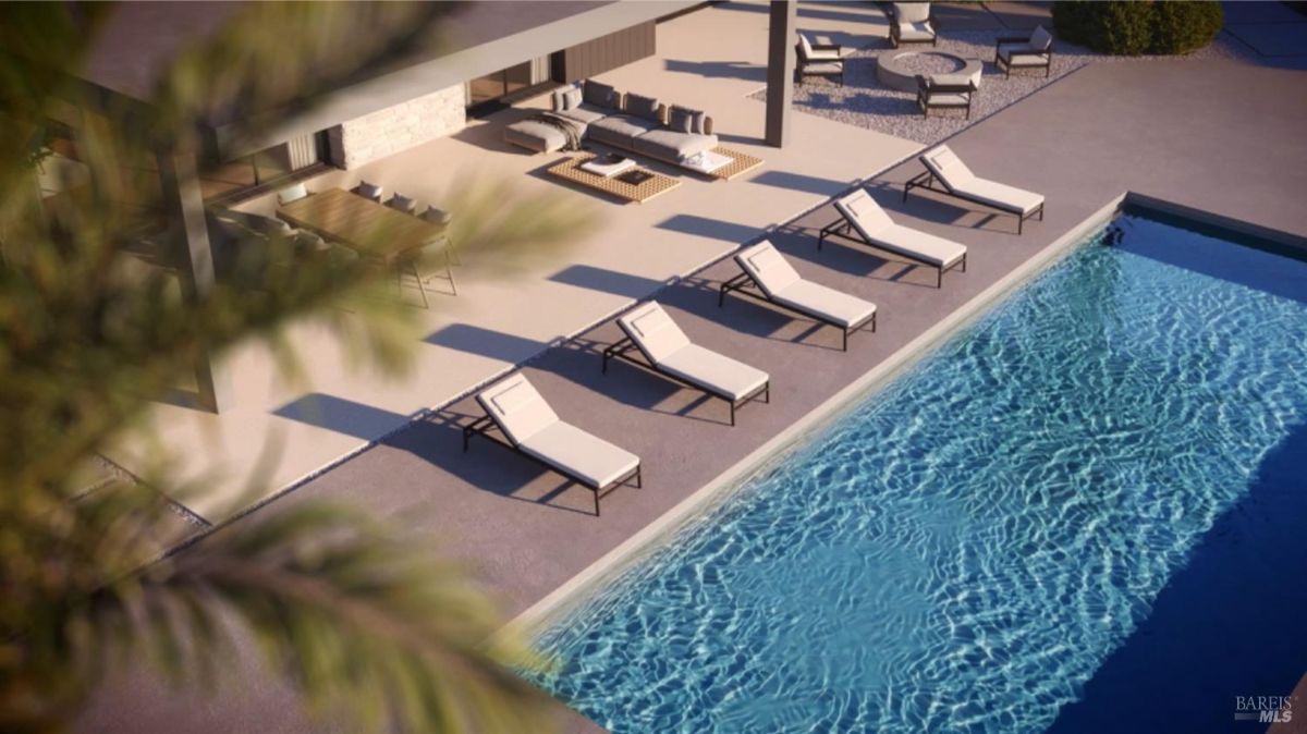 Aerial view of a pool with lounge chairs lined along the deck and a covered patio area featuring a dining and seating setup.