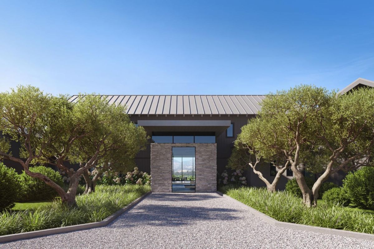 Highlights a front view of the main entrance framed by neatly trimmed greenery and trees. The stone entryway provides a direct line of sight through the home to the outdoor landscape.