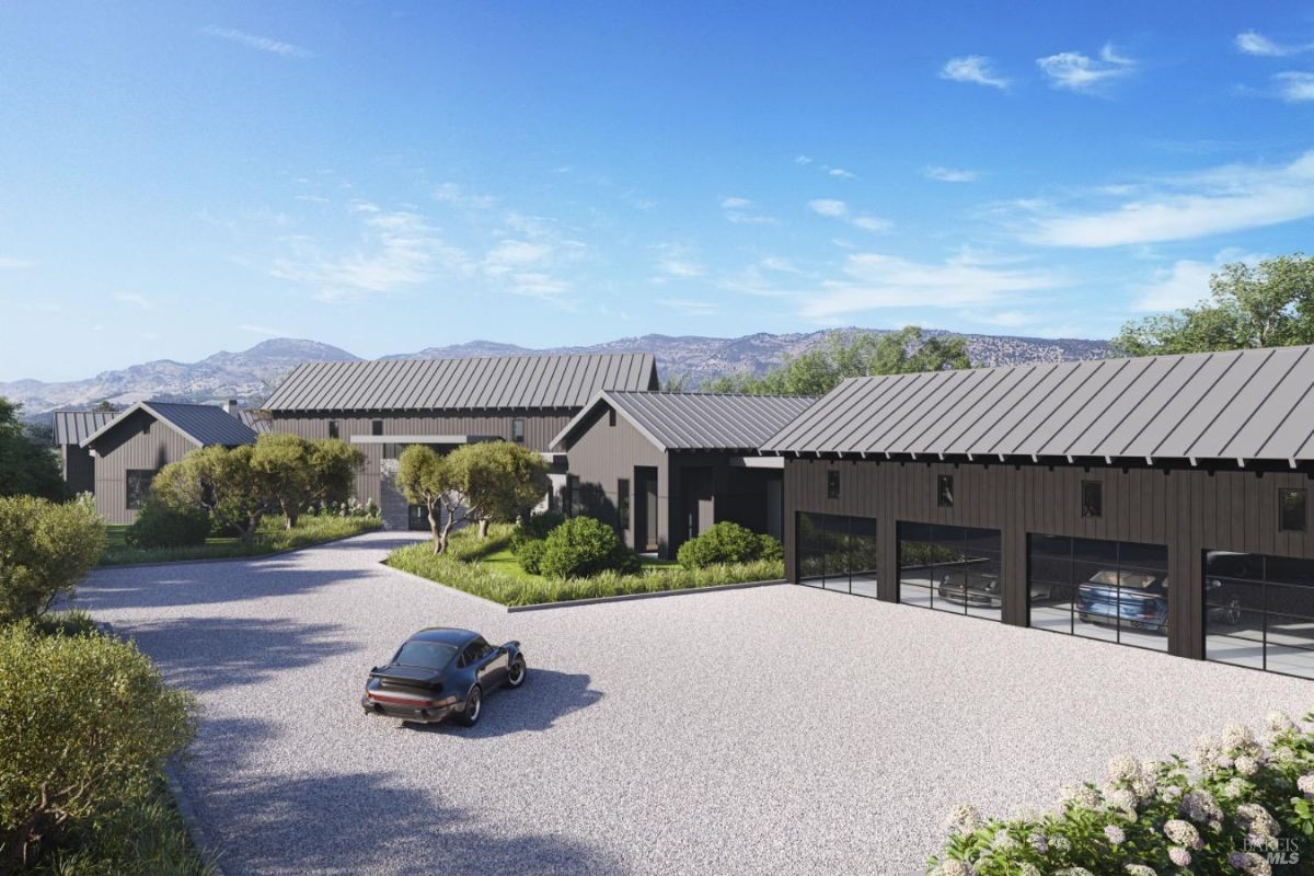 Features a gravel driveway leading to a modern home with metal roofs and a multi-car garage. A single black car is parked in front, surrounded by landscaped greenery and mountain views in the background.