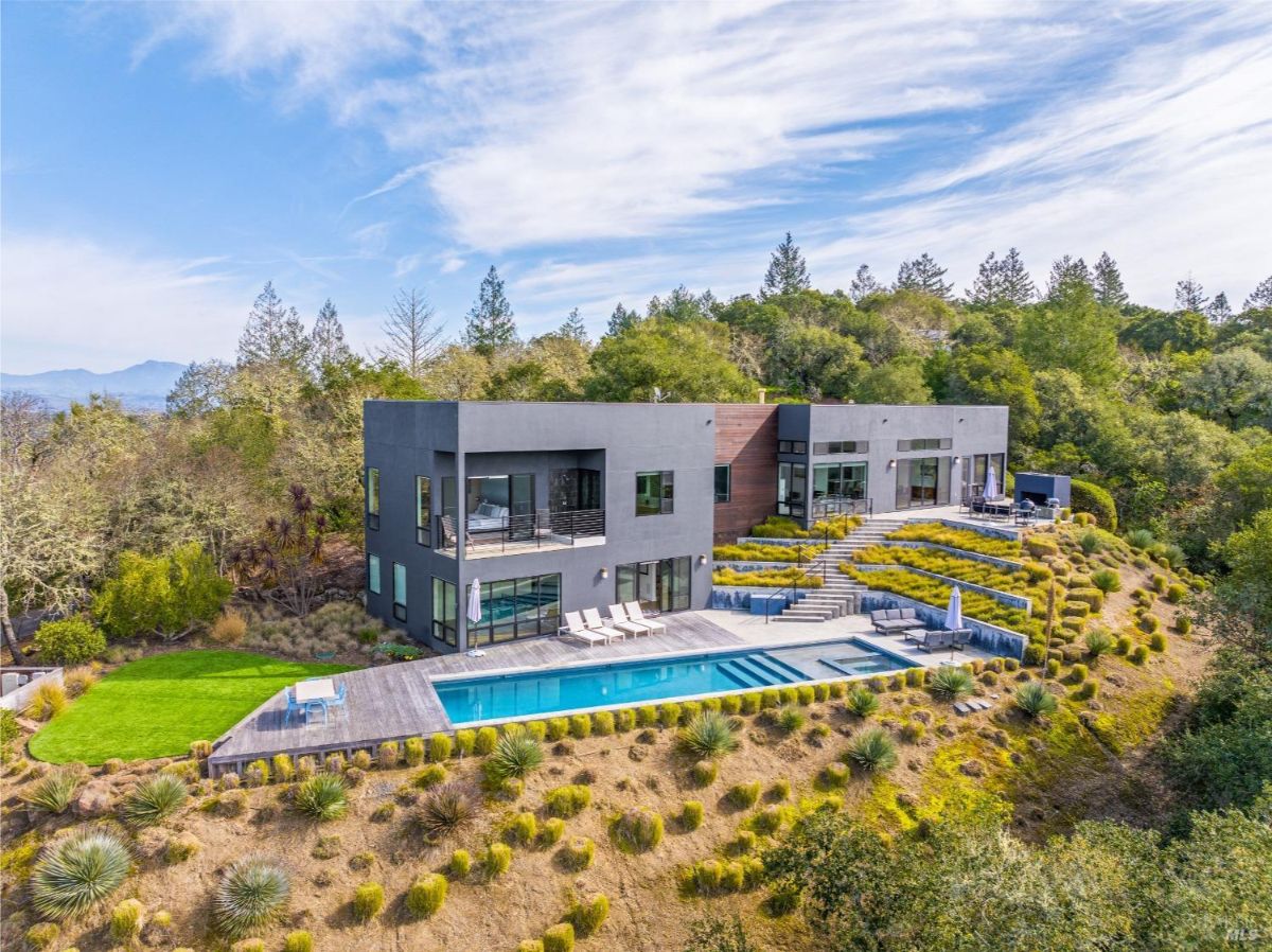 A modern hillside home with a large swimming pool, surrounded by landscaped greenery and natural vegetation.