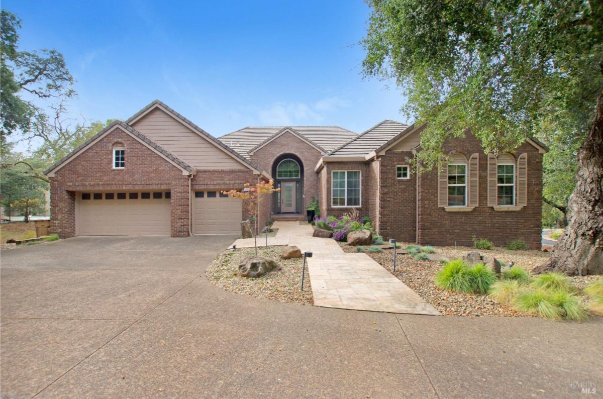 Brick-front house with a three-car garage, landscaped front yard, and a paved walkway leading to the entrance.