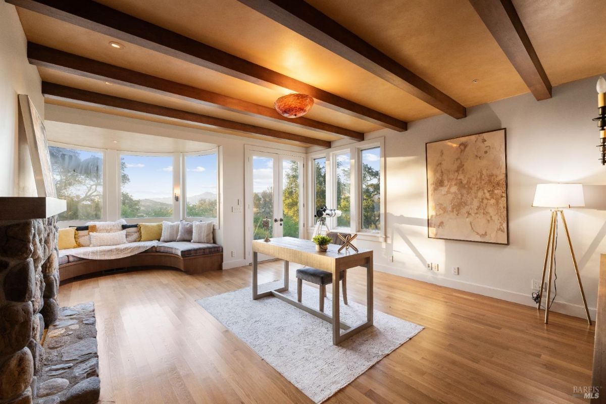 Bright and cozy office space with wood-beam ceilings, a built-in fireplace, and a scenic window seat.