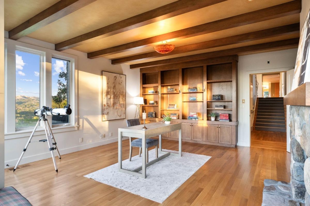 A sophisticated library-style office featuring built-in shelves, a wooden desk, and expansive views of the countryside.