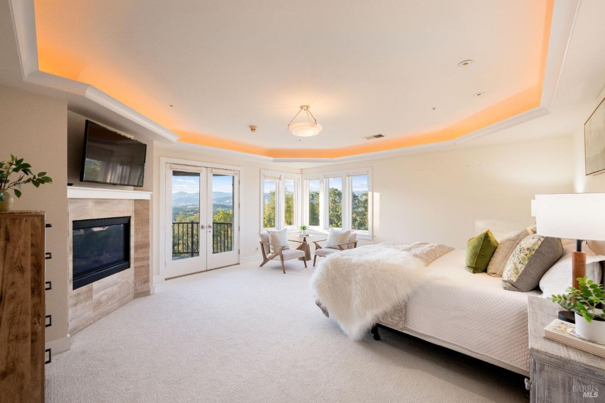 Elegant master bedroom with a curved ceiling, built-in fireplace, and access to a private balcony overlooking picturesque landscapes.