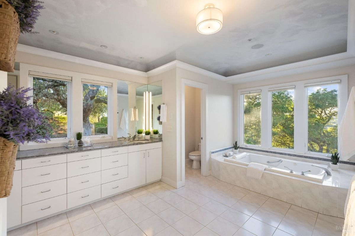 Spacious bathroom featuring double vanity sinks, a soaking tub, and ample natural light from multiple windows.