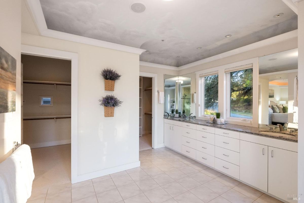 Expansive bathroom showcasing sleek cabinetry, a large mirror, and a serene walk-in closet.