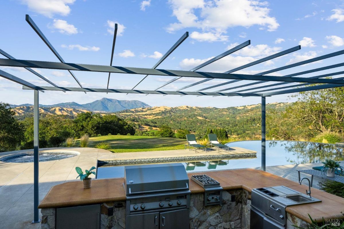 Outdoor kitchen and grill area under a pergola, complemented by a stunning view of the infinity pool and surrounding hills.