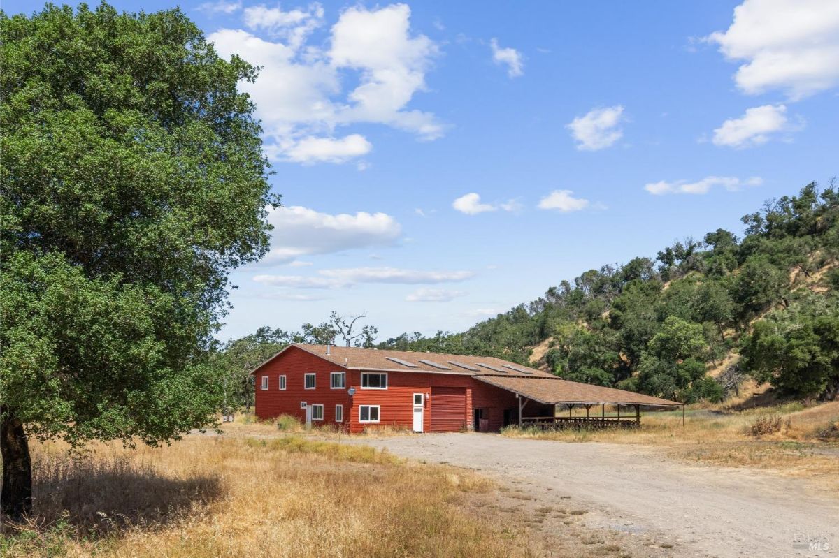 A bright red barn surrounded by trees and hills, ideal for rural or agricultural use.