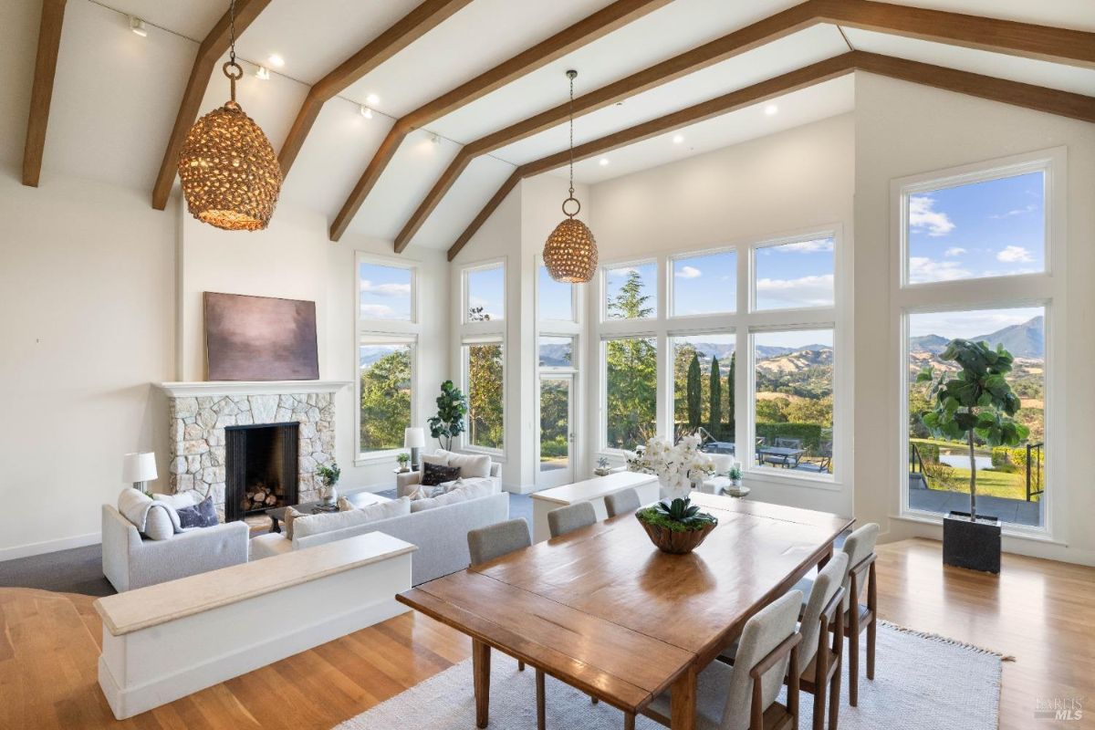  Modern dining room adjacent to a living area, highlighted by a stone fireplace and large windows.