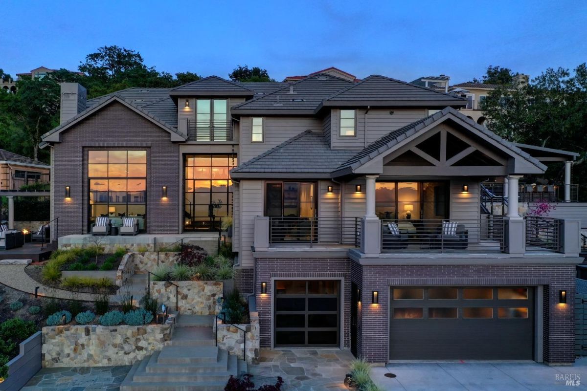 A multi-level modern home with large glass windows, brick and siding exterior, and tiered landscaping in the front yard.