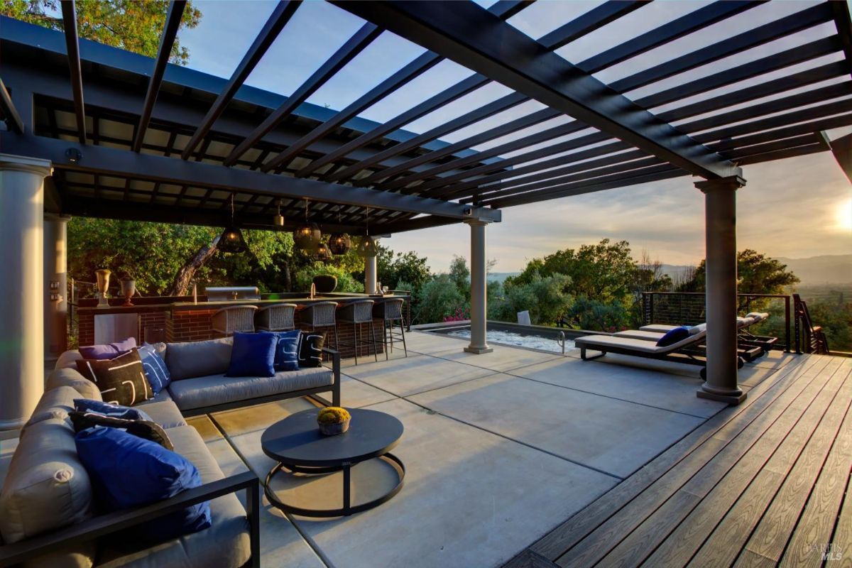 Outdoor seating area featuring a pergola and sectional sofa with bar stools in the background.