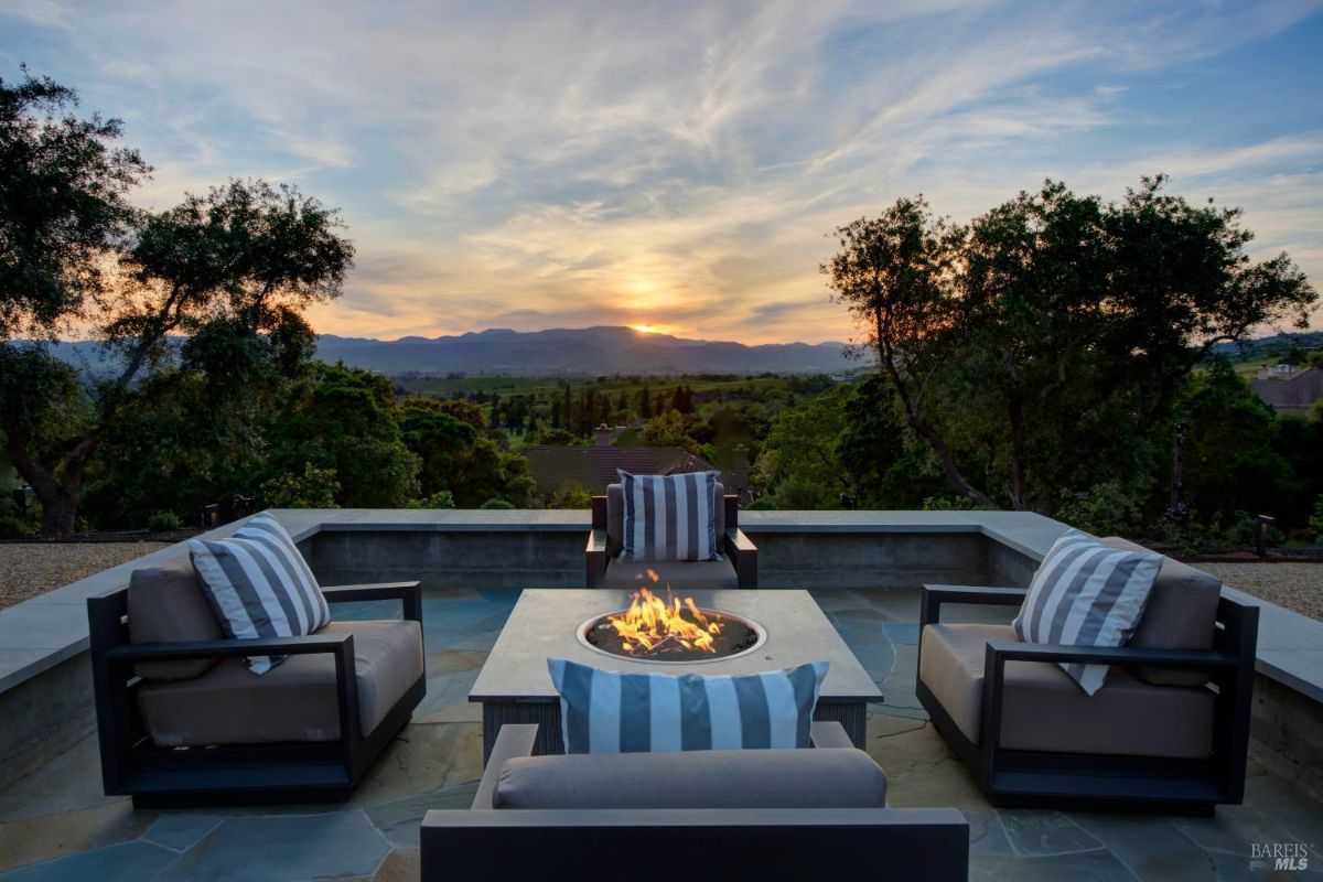 Outdoor seating area with a central firepit overlooking a scenic sunset view.