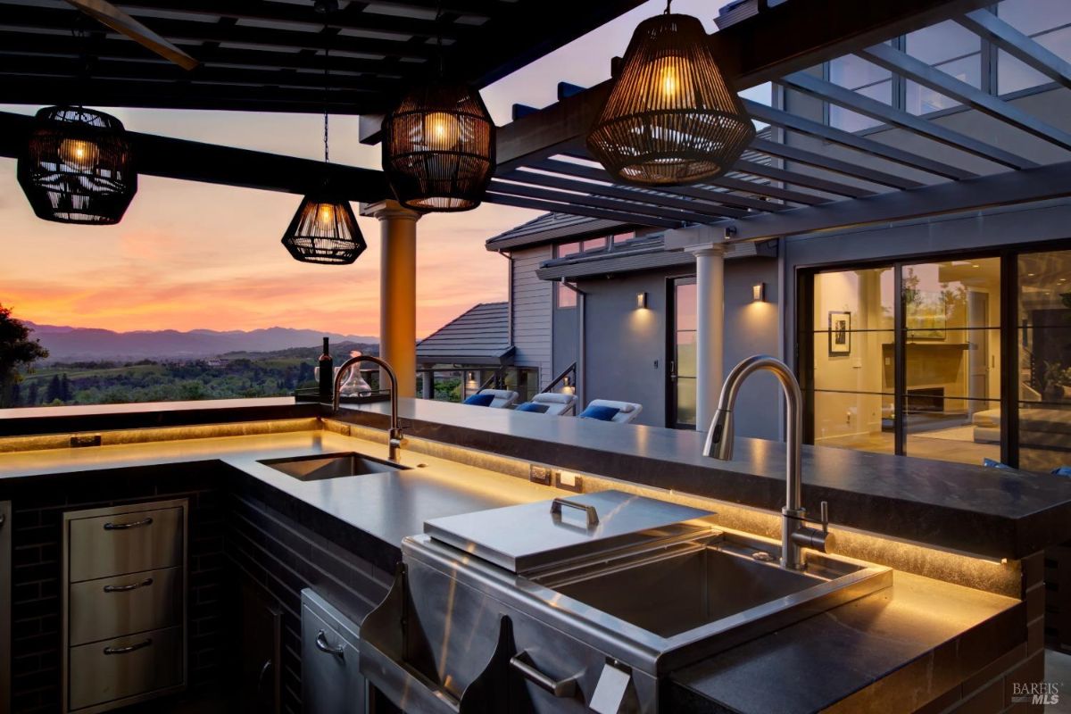 Outdoor kitchen with stainless steel appliances, pendant lighting, and a view of the sunset.