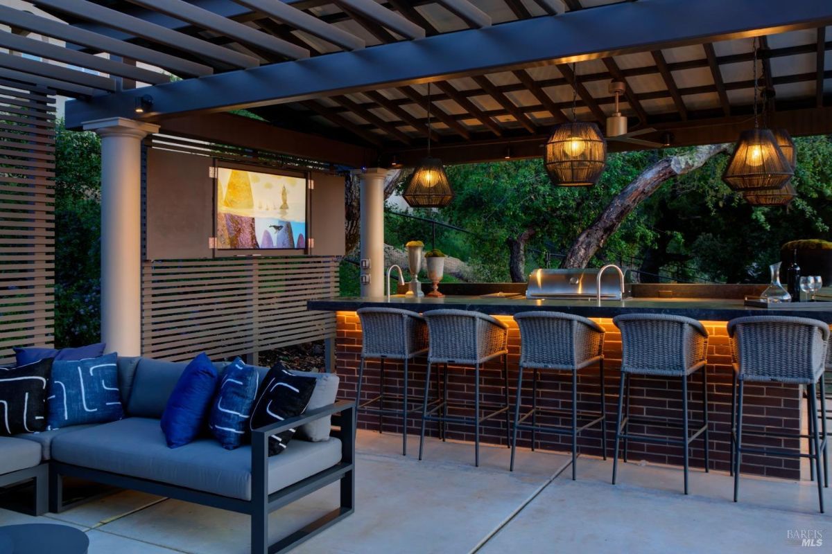 Covered outdoor bar with hanging lanterns, wicker barstools, and a built-in sink