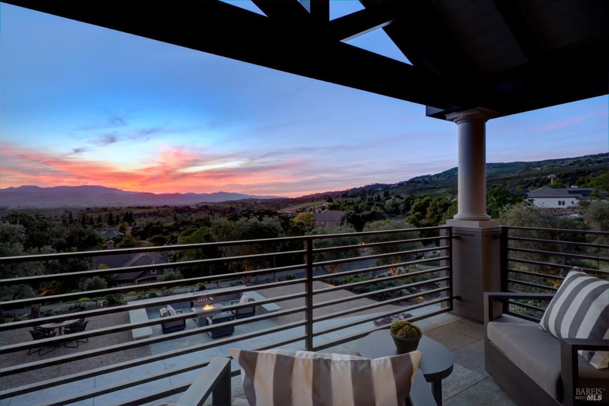 Balcony view with outdoor seating overlooking a sunset and a scenic valley.